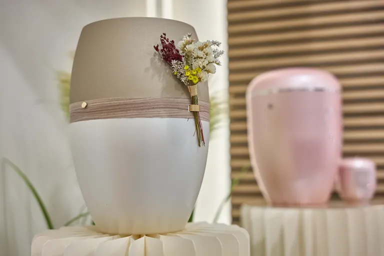 Urne in Taupe und Wei&szlig; mit Trockenblumen-Dekor, im Hintergrund eine rosafarbene Urne